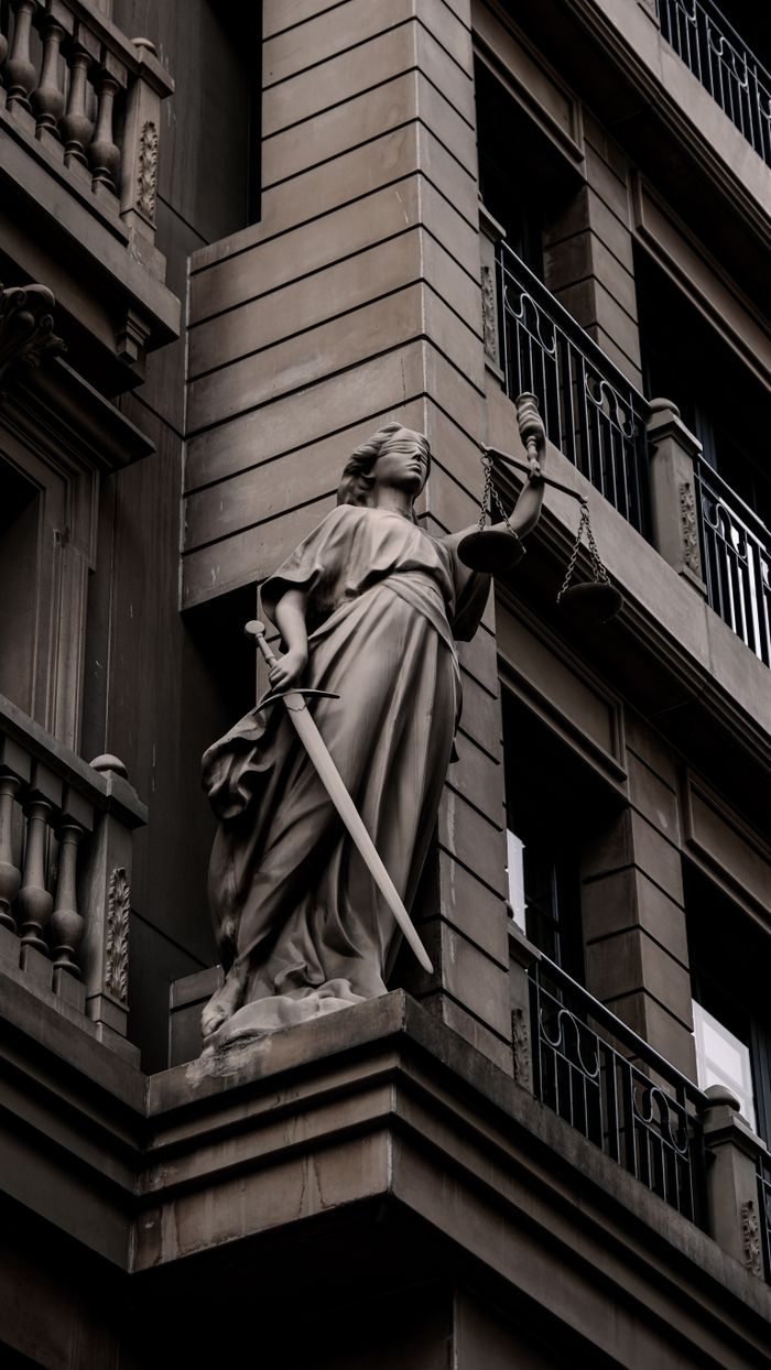 A sculpture of Lady Justice with a sword and scales on a city building's facade.