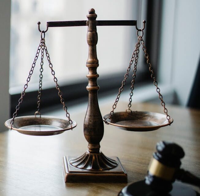 Decorative judgement scale and gavel placed on desk in light lawyer office against window
